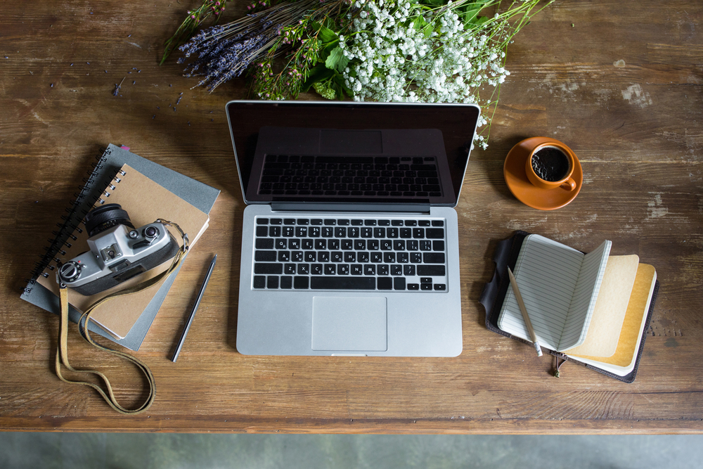 top view of laptop, diaries, vintage photo camera and cup of coffee on wooden tabletop